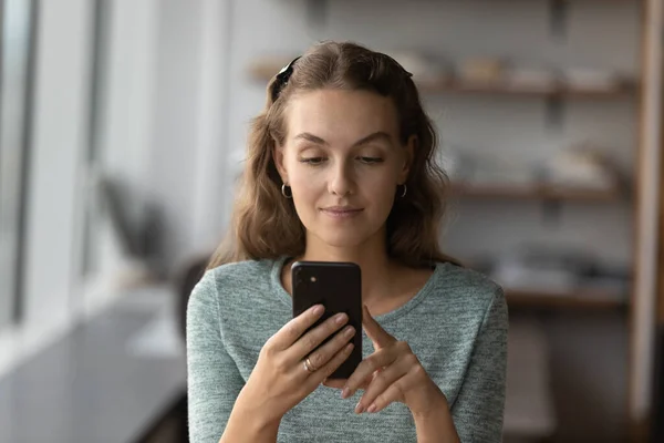 Attractive smiling young woman using smartphone indoors. — Stock Photo, Image