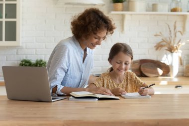 Mutlu genç anne küçük kıza ev ödevinde yardım ediyor..