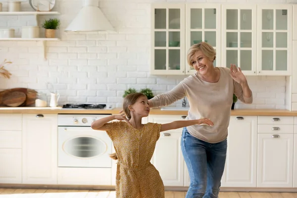 Small child girl dancing with granny in kitchen. — Stock Photo, Image