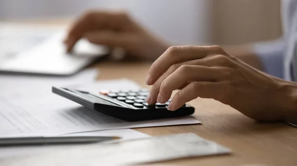 Close up young woman using calculator, managing household monthly budget.