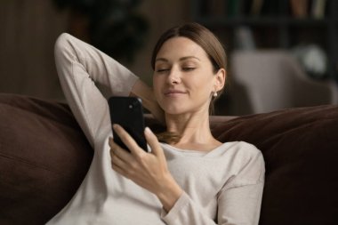 Rahatlamış gülümseyen güzel genç bayan akıllı telefon kullanıyor..