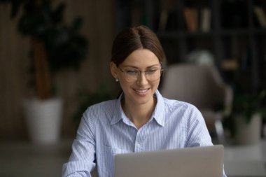 Gözlüklü mutlu genç bayan bilgisayarla çalışıyor..