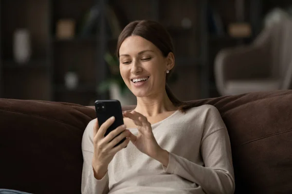 Искренне радостная молодая женщина, пользующаяся сотовым телефоном дома. — стоковое фото