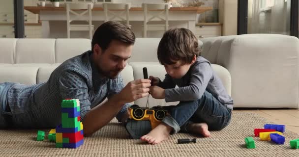 Smiling young daddy helping small son fixing car. — Stock Video