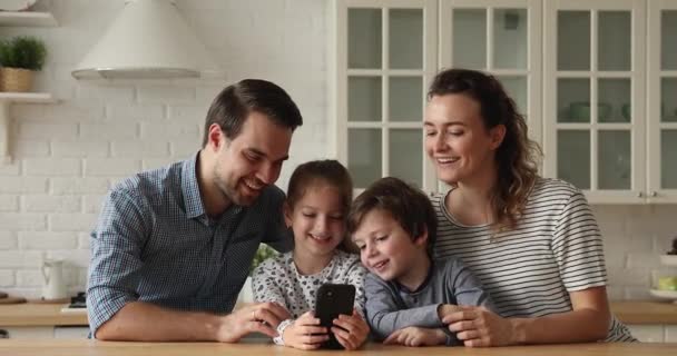 Bonding happy young family couple using smartphone with little children. — стоковое видео