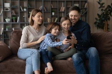 Çocuklu mutlu bir aile evde cep telefonu kullanıyor.