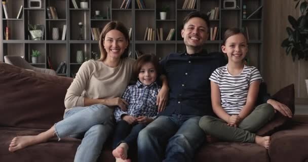 Família com duas crianças sentar no sofá olhar para a câmera — Vídeo de Stock