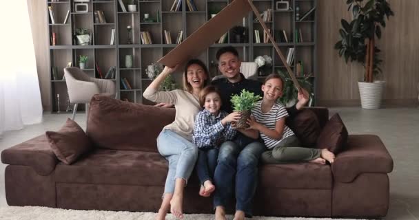 Gifta par med barn sitter på soffan under kartongtaket — Stockvideo