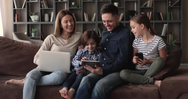 Casal e crianças pequenas relaxar no sofá usando diversos dispositivos — Vídeo de Stock