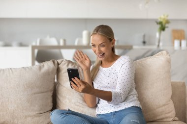 Heyecanlı kadın el sallıyor, akıllı telefondan video görüşmesi yapıyor.