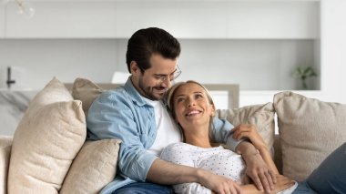 Mutlu genç evli çift sarılıyor, rahat bir kanepede dinleniyorlar.