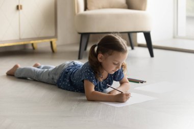 Sevimli küçük kız yere renkli kalemler çiziyor.