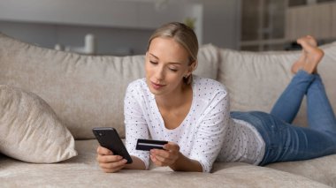 Kredi kartı ve akıllı telefon ödemesi yapan tatmin olmuş genç bir kadın.