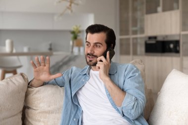 Telefonla konuşan gülümseyen adam evdeki koltukta oturuyor.