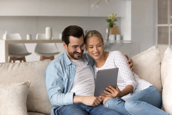Feliz joven pareja usando la tableta, abrazos relajante en el sofá juntos —  Fotos de Stock
