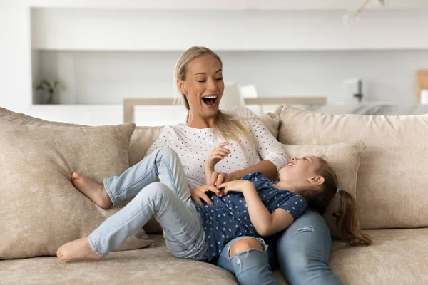 Alegre madre e hija divirtiéndose, cosquillas en el sofá — Foto de Stock