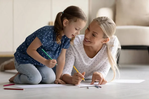 Feliz madre amorosa y pequeña hija dibujo, acostado en el suelo —  Fotos de Stock