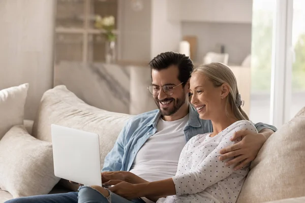 Happy wife and husband hugging, relaxing on couch with laptop