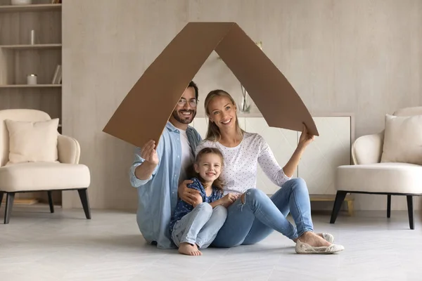 Família feliz com adorável filhinha sentada sob teto de papelão — Fotografia de Stock
