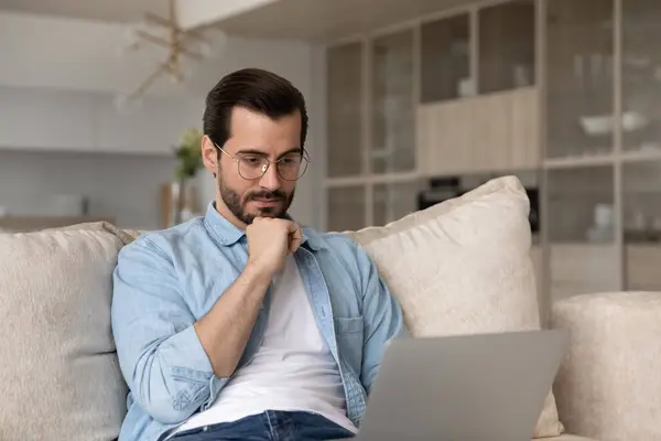 Gözlüklü düşünceli adam dizüstü bilgisayara bakıyor, internette çalışıyor. — Stok fotoğraf
