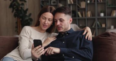 Çift kanepeye oturur, akıllı telefon kullanır. Yeni mobil uygulamanın keyfini çıkarırlar.