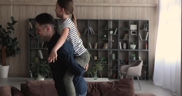 Игривый отец таскает дочь на спине в гостиной — стоковое видео