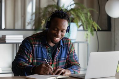 Gülümseyen Afro-Amerikan kulaklıklı adam not alıyor, internetten çalışıyor.