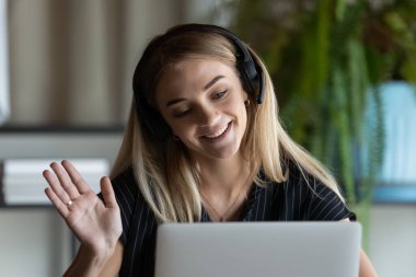 Kulaklıklı iş kadını dizüstü bilgisayara el sallıyor.