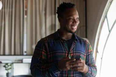 Gülümseyen Afro-Amerikan iş adamı ofisteki akıllı telefondan dikkati dağılıyor.