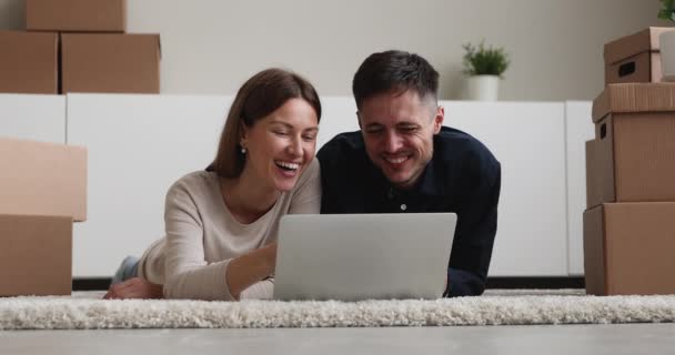 Casal deitado perto de caixas de papelão usando laptop escolher serviços móveis — Vídeo de Stock