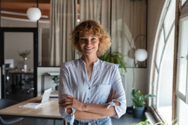 Kollarını kavuşturmuş gülümseyen bir iş kadını portresi.