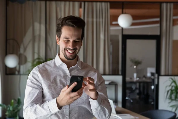 Head shot uomo d'affari sorridente utilizzando smartphone in piedi nella stanza dell'ufficio — Foto Stock