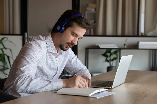 Employee in headphones taking notes, watching webinar in office — Stock Photo, Image