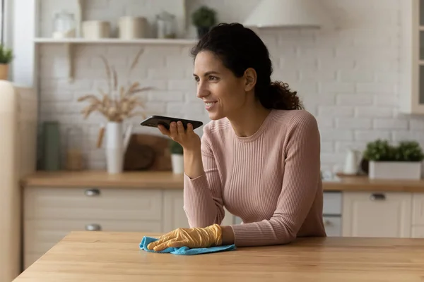 Счастливая молодая женщина отправляет аудиосообщение во время уборки кухни. — стоковое фото
