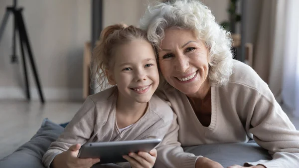 Nenek yang sudah pensiun dan cucu perempuannya bersantai di atas bantal memegang tablet — Stok Foto