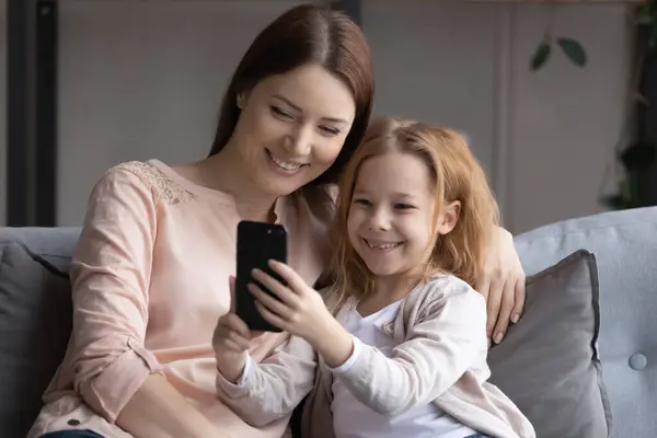 Усміхнена дівчина сидить на дивані використовуйте смартфон з матір'ю — стокове фото