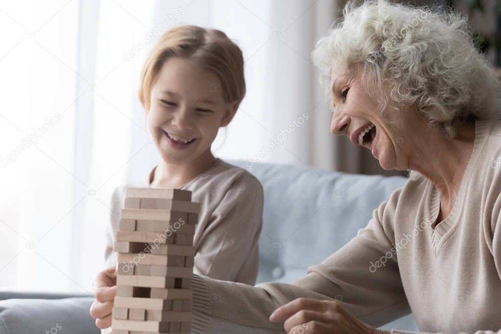 Laughing senior grandmother enjoy playing board game with little granddaughter