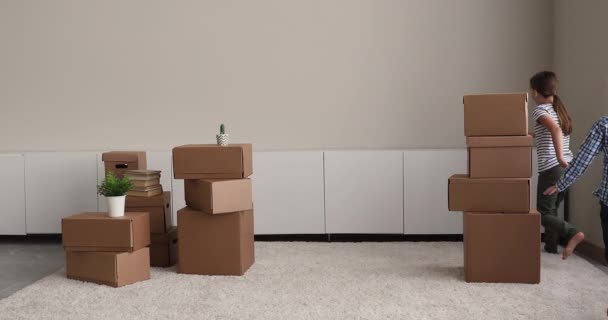 Siblings play catch up in living room around boxes indoor — Stock Video