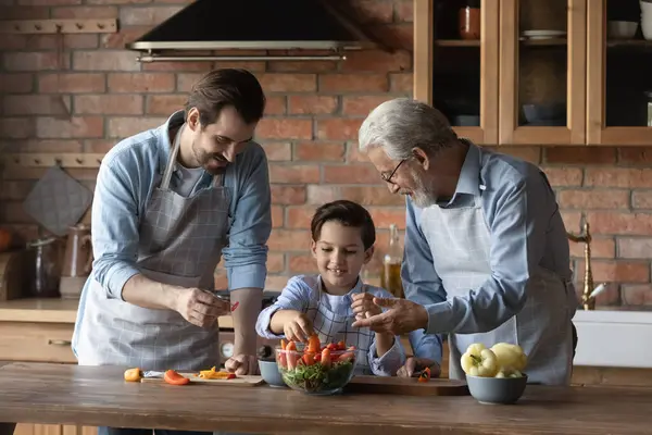 Mutlu baba ve büyükbaba çocuklara salata yapmayı öğretiyor. — Stok fotoğraf