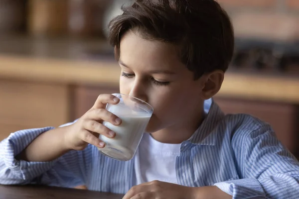 学龄前男孩在厨房吃早餐时喝玻璃杯牛奶 — 图库照片