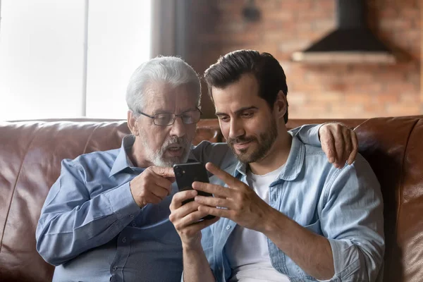 Hijo adulto enseñando a papá de 70 años de edad a usar la aplicación móvil — Foto de Stock