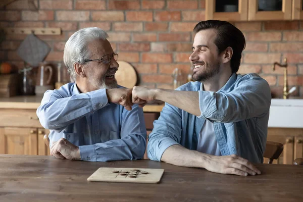 Happy elderly dad and grownup son giving fist bumps — Stock Photo, Image