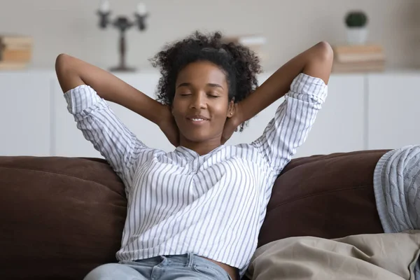 Huzurlu gülümseyen Afro-Amerikan kadın kanepeye yaslanıyor. — Stok fotoğraf