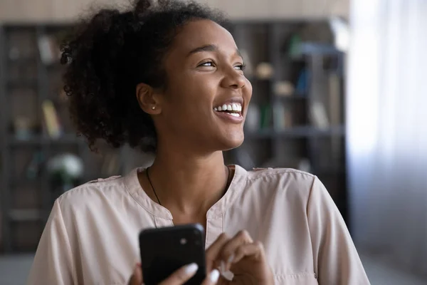 De cerca sonriente mujer afroamericana soñadora sosteniendo teléfono inteligente — Foto de Stock