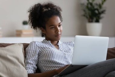 Kanepede dizüstü bilgisayar kullanan tatmin olmuş Afrikalı Amerikalı kadın.