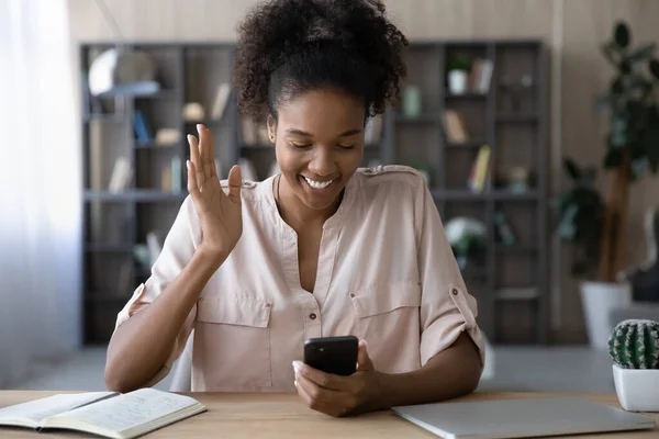 Sonriendo mujer afroamericana agitando la mano, sosteniendo el teléfono inteligente, charlando en línea — Foto de Stock