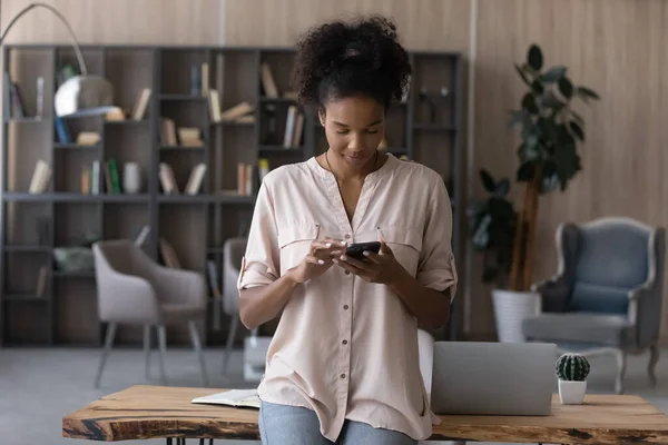 Femme afro-américaine confiante utilisant un smartphone, debout près du bureau — Photo
