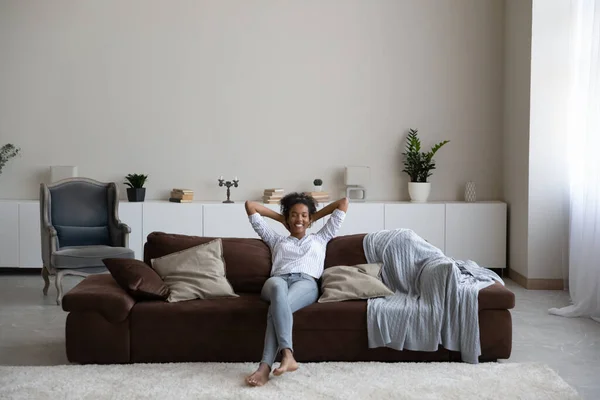 Femme afro-américaine souriante se reposant sur un canapé confortable — Photo