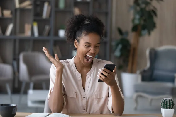 Задоволена афроамериканкою, яка радіє успіхам, тримає смартфон, читає новини — стокове фото