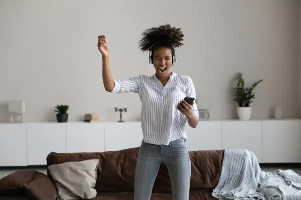Feliz millennial mujer afroamericana en auriculares bailando, sosteniendo teléfono inteligente — Foto de Stock